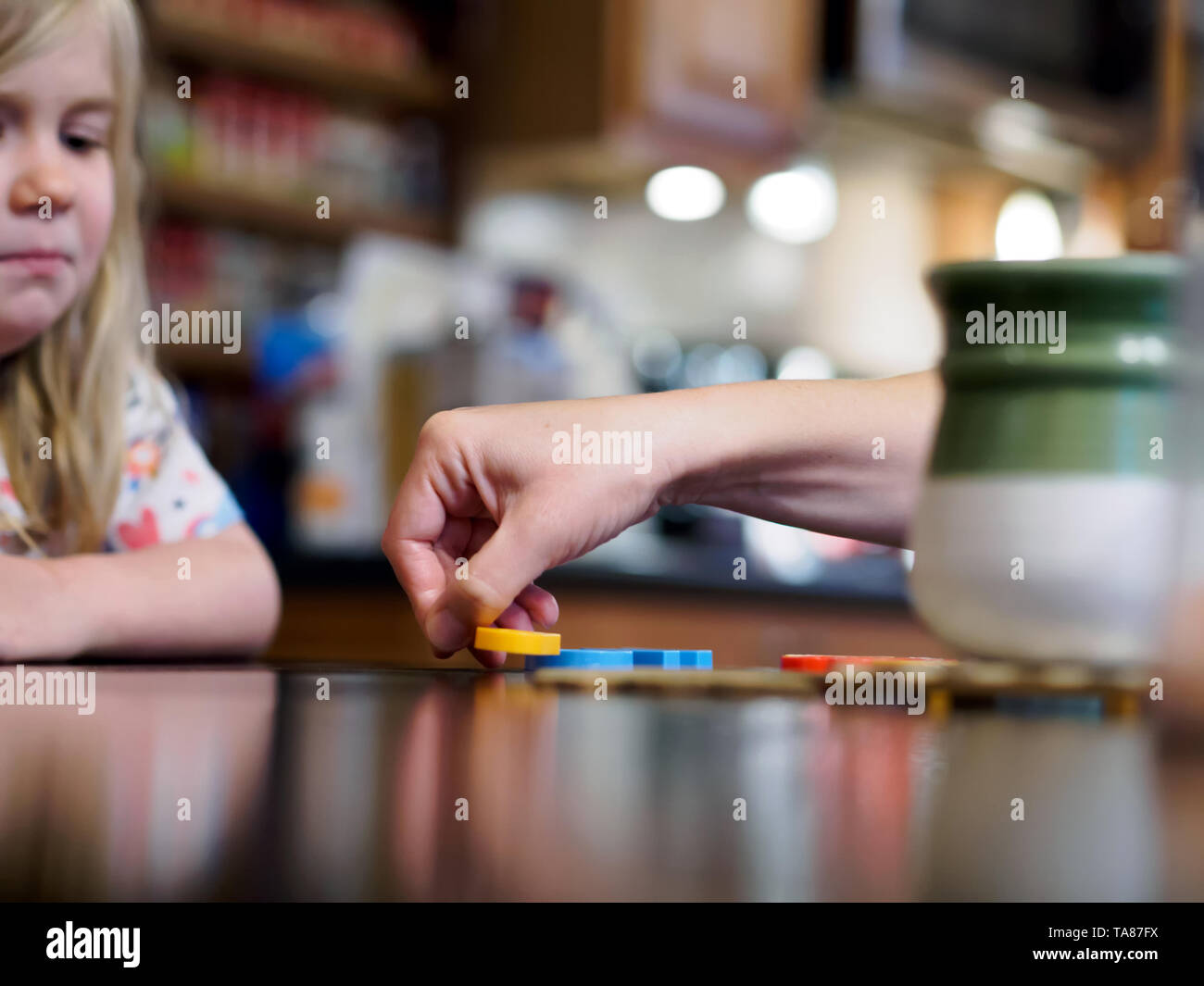 Mütter Hand ordnet Kunststoff Buchstaben in Wörtern auf einem Küchentisch während junge Tochter auf von Kante der Rahmen sieht. Flache Freiheitsgrad. Stockfoto