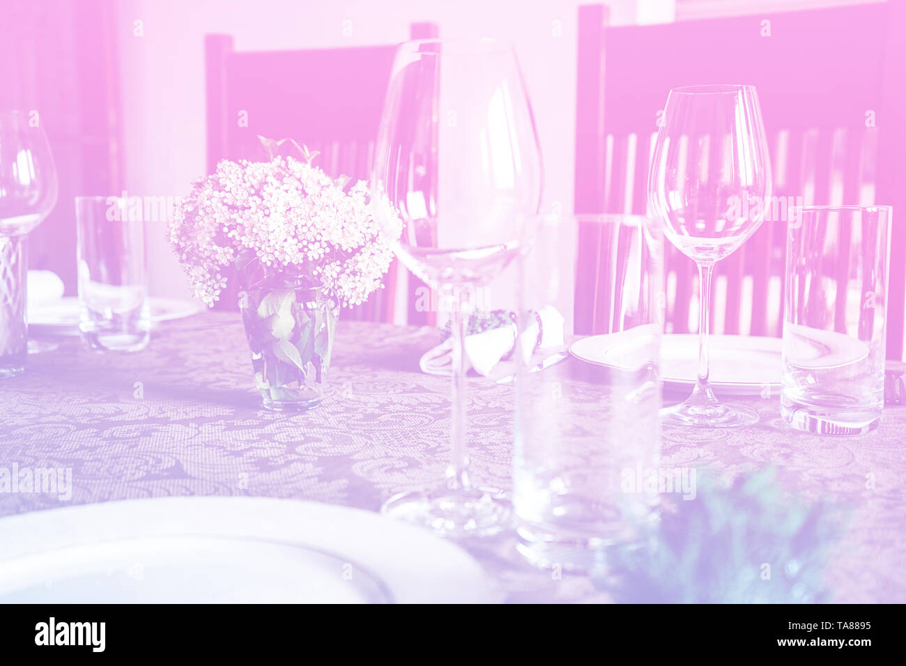 Wein Glas bei der Feier und Esstisch mit Blumen Dekorationen auf Hellrosa blauen Gradienten Hintergrund. Stockfoto