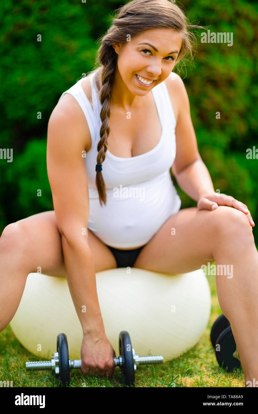 Lächelnd schwangere Frau Hanteln beim Sitzen auf Yoga Ball Stockfoto