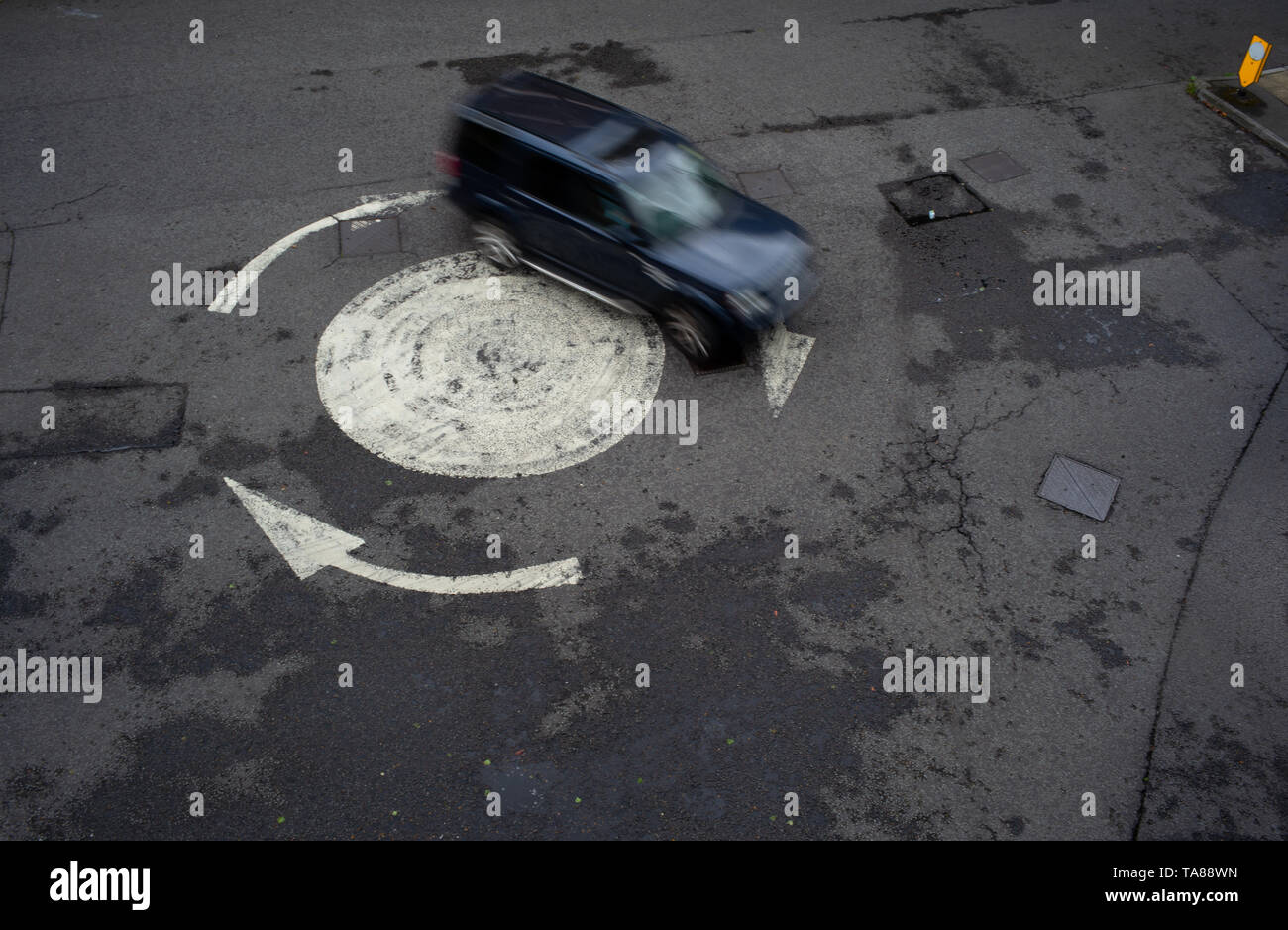 Luftaufnahme von einem lackierten Pfeil Kreisverkehr mit einem einzigen Auto herum zu gehen. Könnte als eine Analogie oder Konzept als verloren oder Going In Circles verwendet werden. Stockfoto
