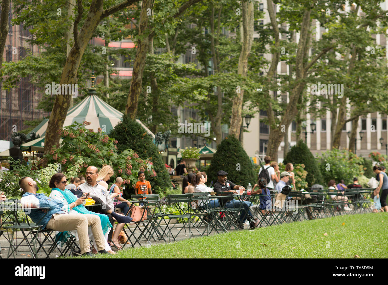 Gruppe von Menschen sitzen im Bistro Tische auf den Pfad entlang Rasen, Bryant Park, New York City, New York, USA Stockfoto
