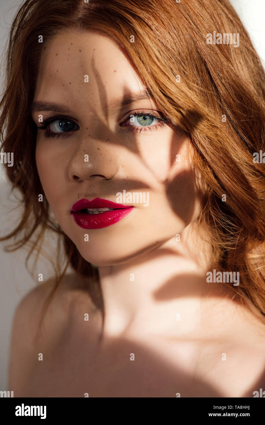 Schöne junge rothaarige Frau mit roten Lippen und Schatten im Gesicht an Kamera Stockfoto