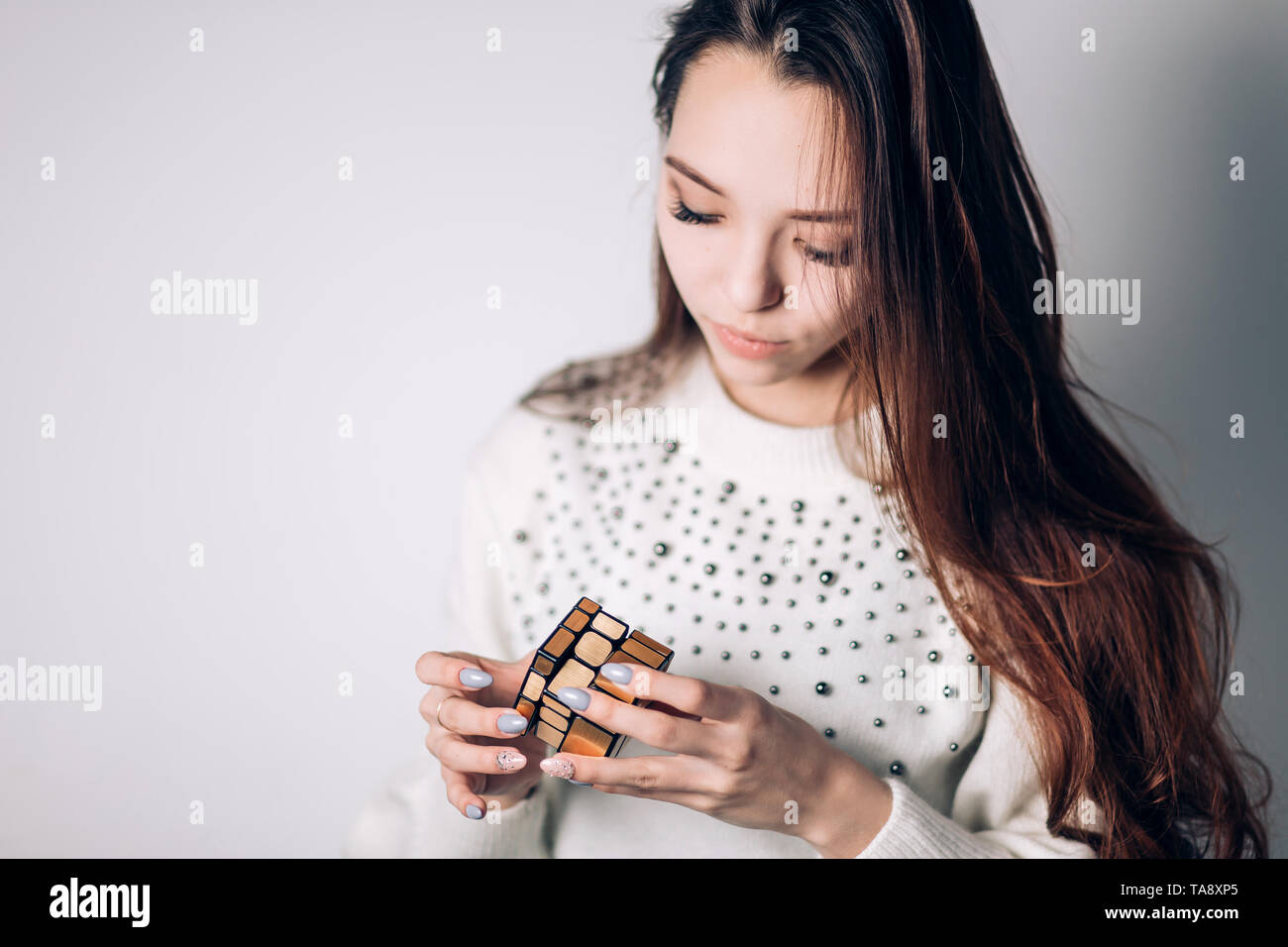 UFA, Russland - Januar 14, 2018: Eine schöne Brünette Frau in einem weißen Pullover sammelt ein Puzzle, Cube ein Spiegel Golden Rubik's auf einem weißen Hintergrund. F Stockfoto