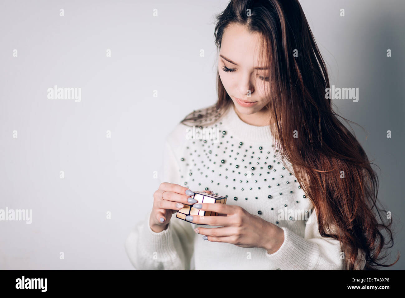 UFA, Russland - Januar 14, 2018: Eine schöne Brünette Frau in einem weißen Pullover sammelt ein Puzzle, Cube ein Spiegel Golden Rubik's auf einem weißen Hintergrund. Stockfoto