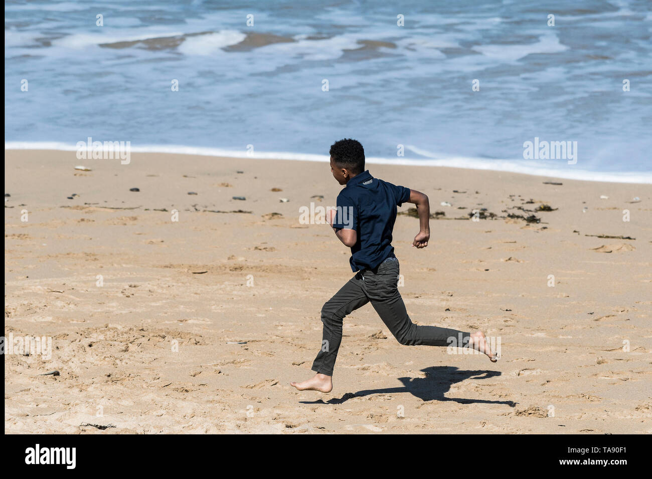 Ein junger Teenager begeistert läuft an einem sonnigen Tag an Fistral Beach in Newquay in Cornwall. Stockfoto