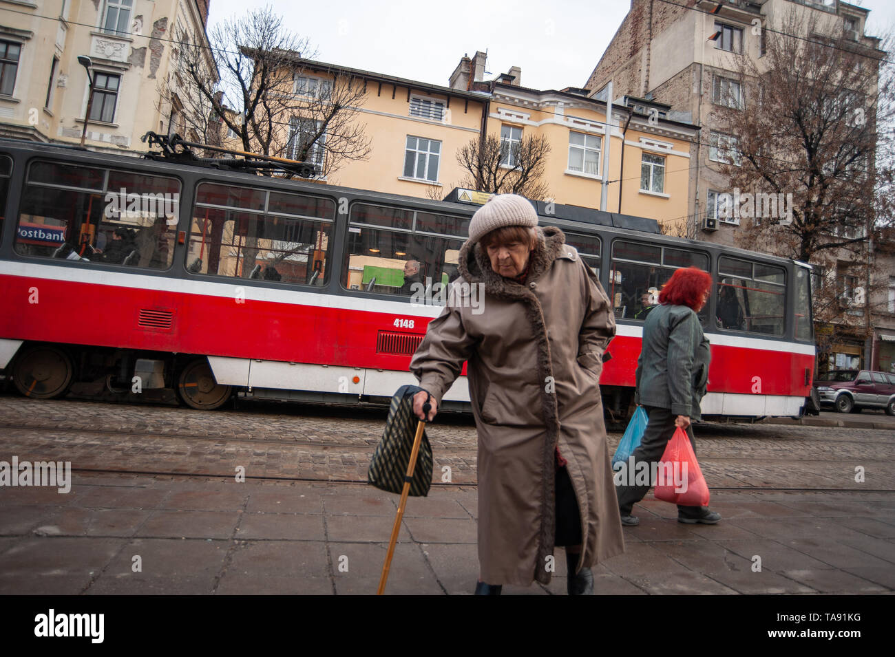 Eine alte bulgarische Frauen überquert die Straße an einer Straßenbahnhaltestelle im Zentrum von Sofia, Hauptstadt von Bulgarien Stockfoto