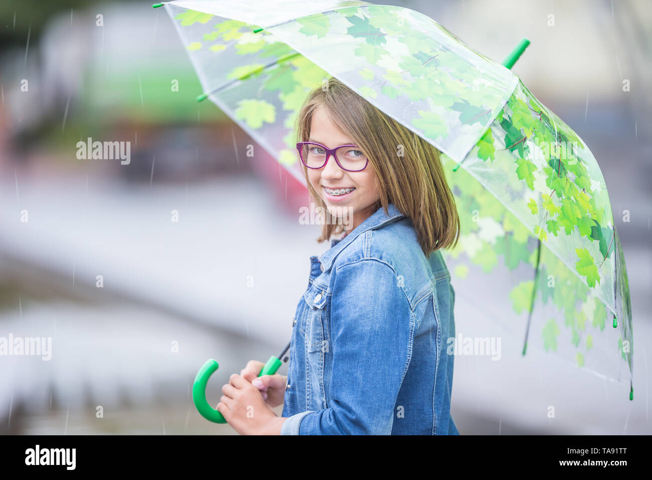 Portrait von schönen Jungen vor - jugendlich Mädchen mit Regenschirm im Frühjahr oder Sommer Regen. Stets lächelndes Mädchen mit Zahnspangen und Gläser. Stockfoto