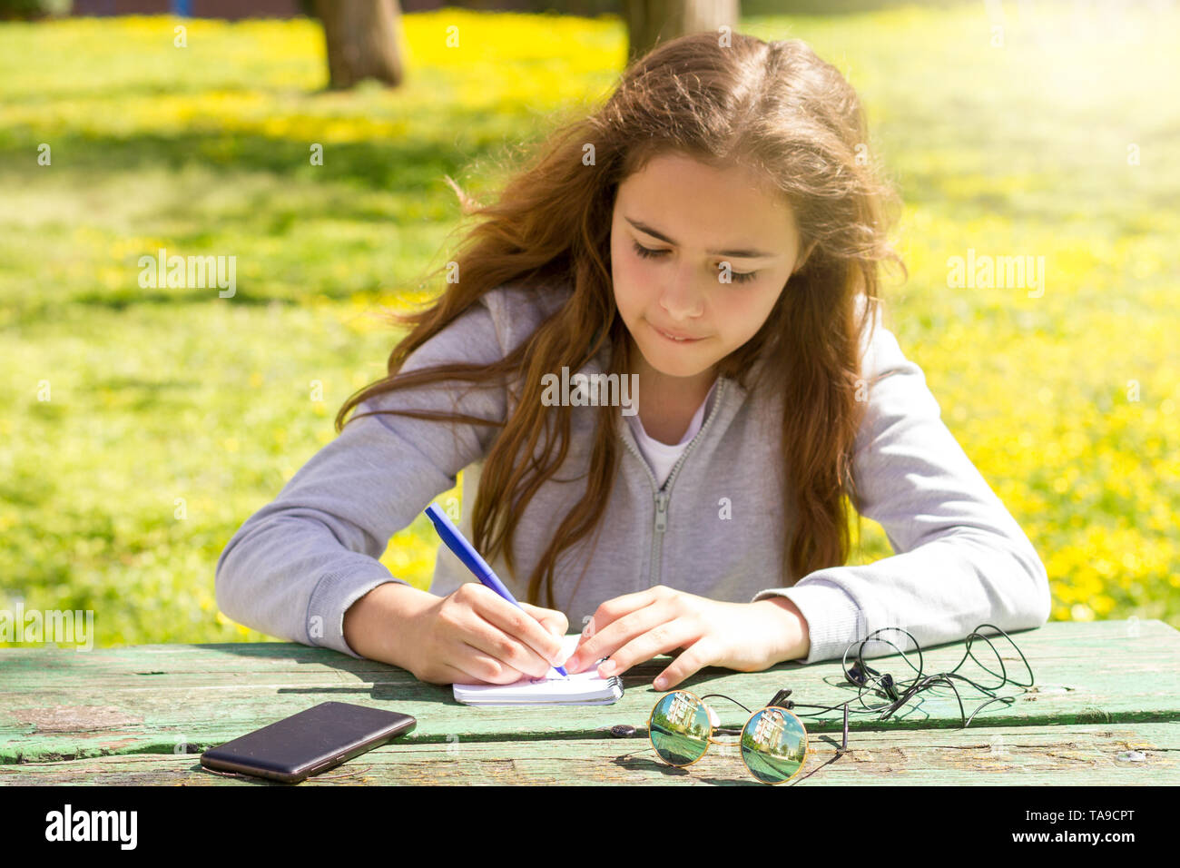 Cute Teen Girl schreibt Notizen auf einem Papierblock durch hölzerne Tabelle auf der grünen Wiese Stockfoto