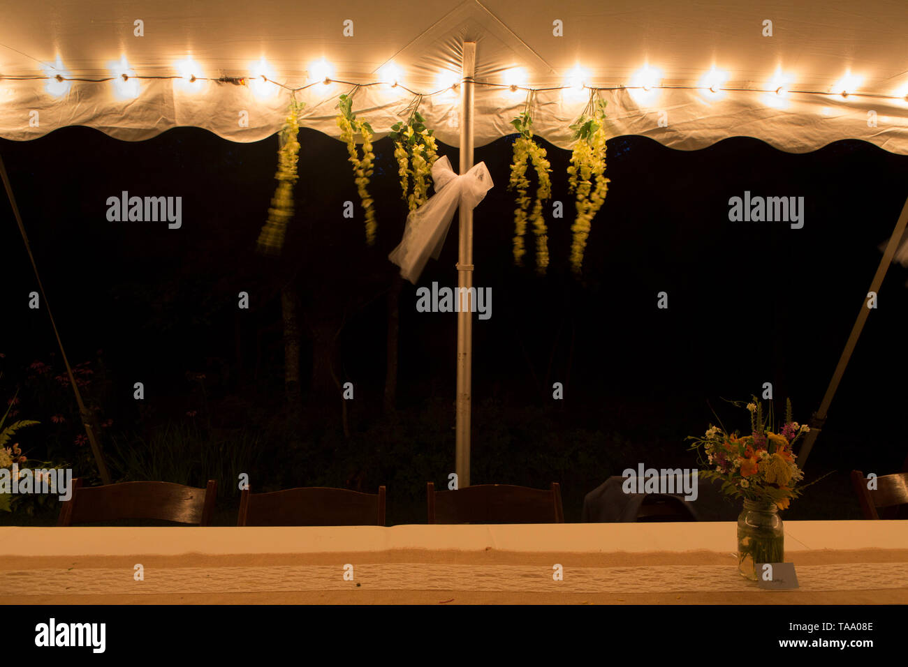 Leeres Zelt mit Hochzeit Dekorationen beleuchtet, langen Tisch und Strauß Blumen in der Nacht Stockfoto