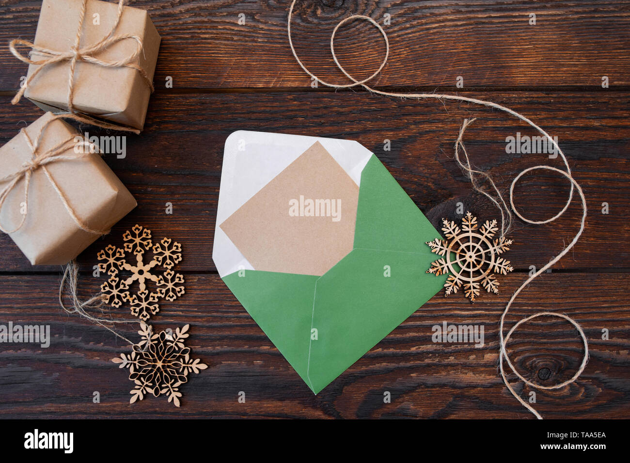 Weihnachtsmockup Urlaubsbrief Blank Papier in grünen Umschlag mit hölzernen Schneeflocken und Geschenkboxen auf Holztisch, mit Platz für Ihren Text, Draufsicht Stockfoto