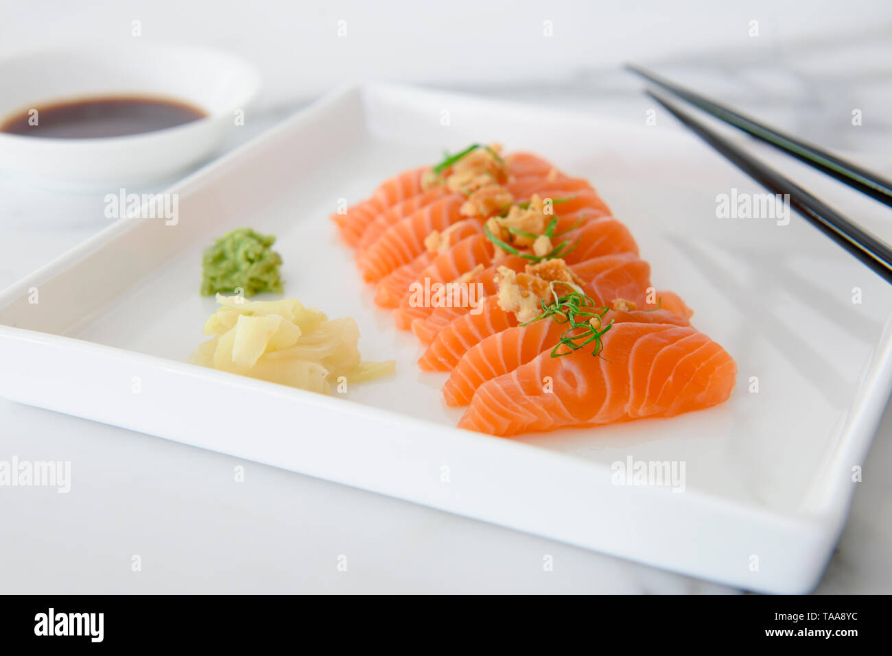 Frisch geschnittene Lachs-sashimi mit Wasabi, eingelegten Ingwer und Sojasauce die Seite auf weiße Platte mit Stäbchen Stockfoto