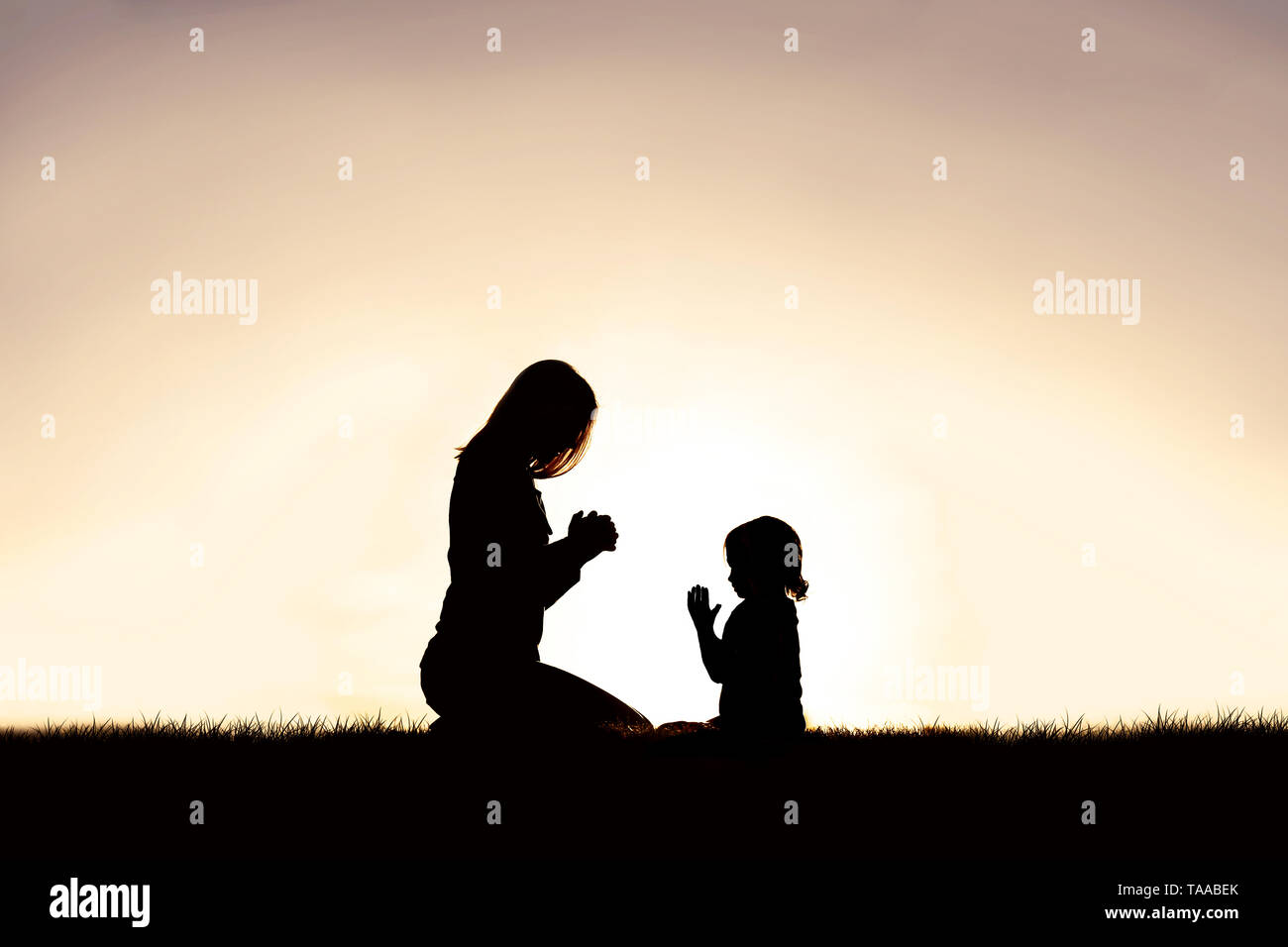 Die Silhouette eines christlichen Mutter ihr Kind zu beten, wie sie friedlich draußen sitzen, gegen den Sonnenuntergang in den Himmel. Stockfoto