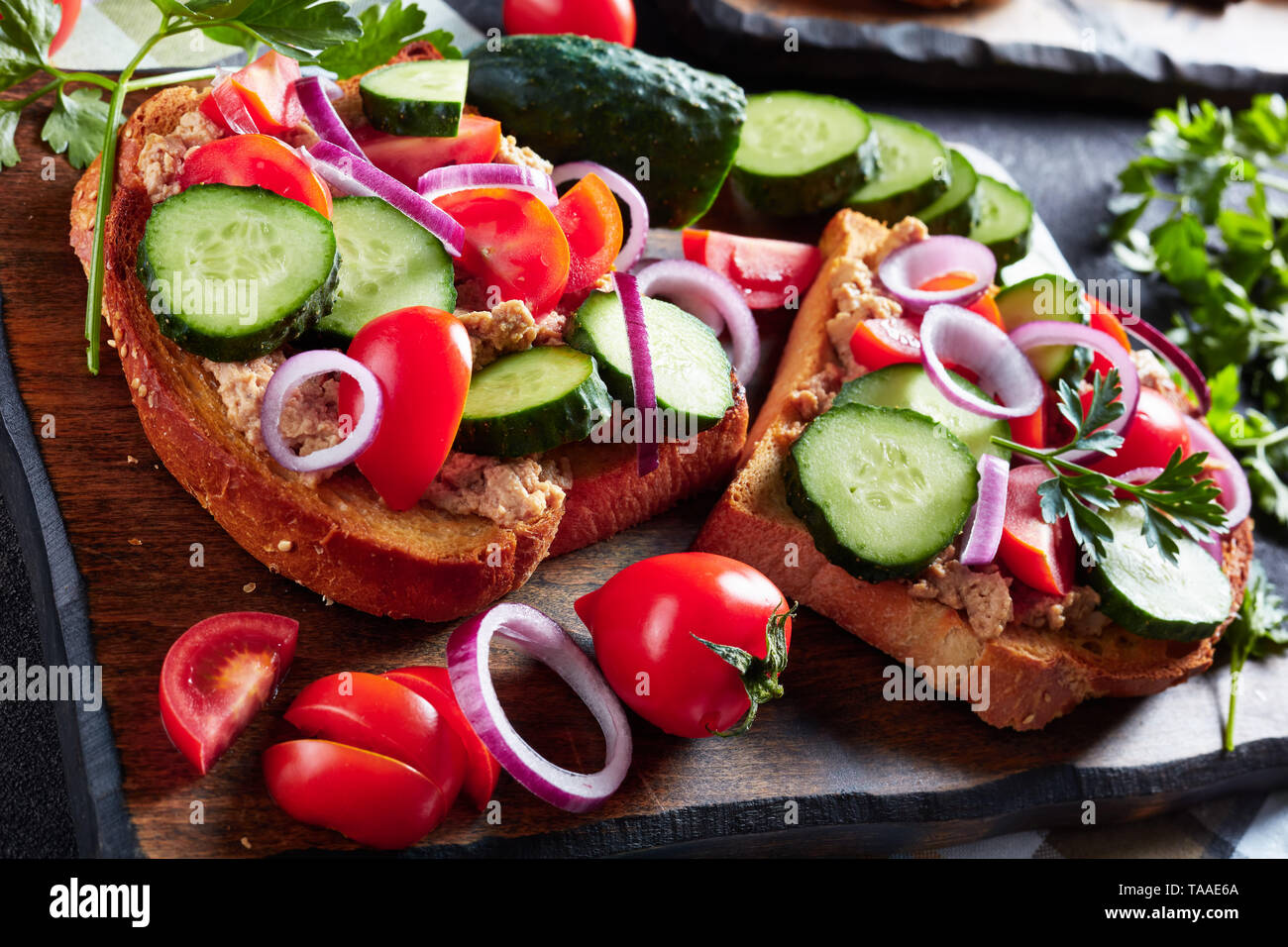 Sandwiches mit Lebertran Pastete, mit geschnittenen Gurken, Tomaten und roter Zwiebel Ringe auf einem Schneidebrett mit Zutaten auf einem Küchentisch überstieg, Stockfoto