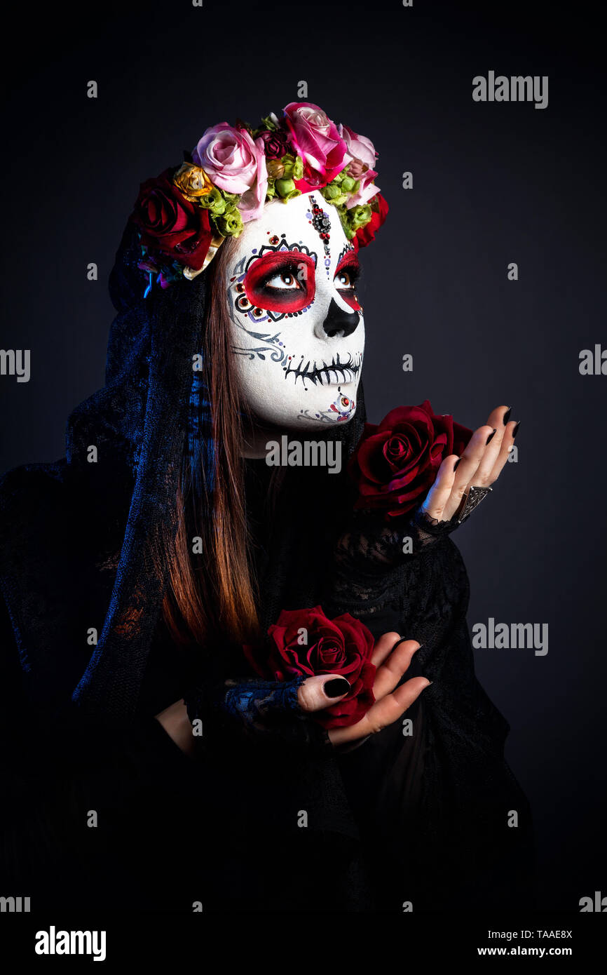 Mädchen mit Sugar Skull mit rosa Blüten feiert Tag der Toten auf schwarzen Hintergrund machen Stockfoto