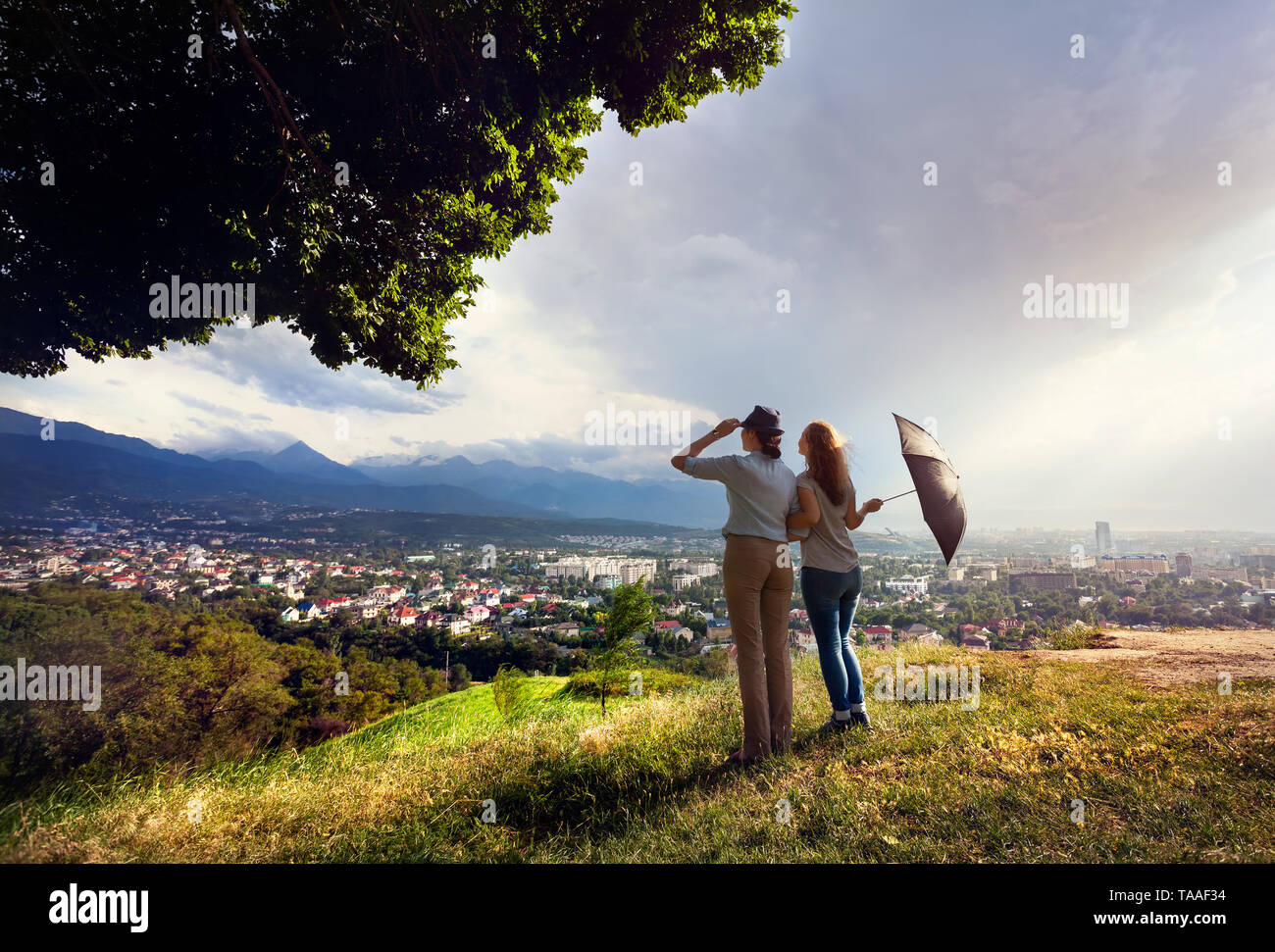 Zwei Freunde mit Schirm zu den schönen Blick auf die Stadt Panorama in die Berge bei regnerischen dramatischer Sonnenuntergang Stockfoto