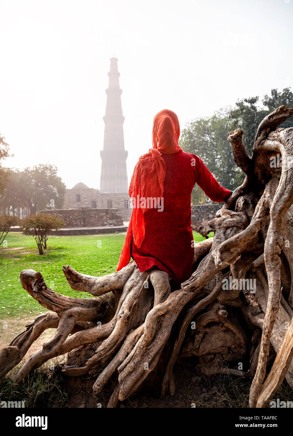 Frau in rot Kostüm sitzen auf den Stumpf und Qutub Minar Turm in Old Delhi, Indien Stockfoto