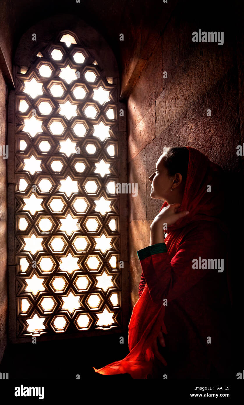 Frau in rot Indischen rotes Kleid mit Schal auf dem Balkon in der Nähe von Mosaik Fenster im Palast in Indien Stockfoto