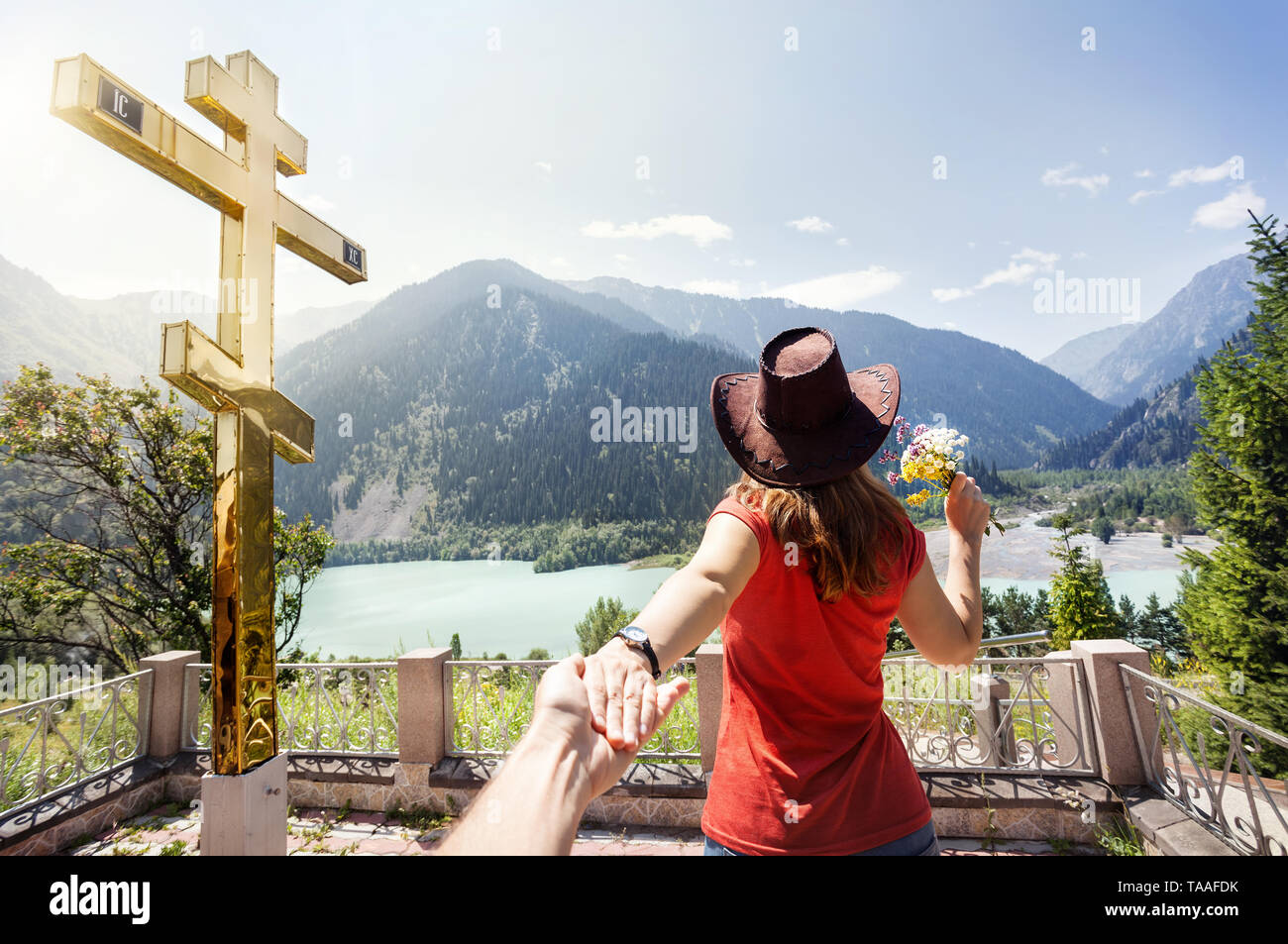 Touristische Frau mit Hut mit einem Mann an der schönen Aussicht auf die Berge See in den Bergen in der Nähe von grossen Goldenen Kreuz in Kasachstan Stockfoto
