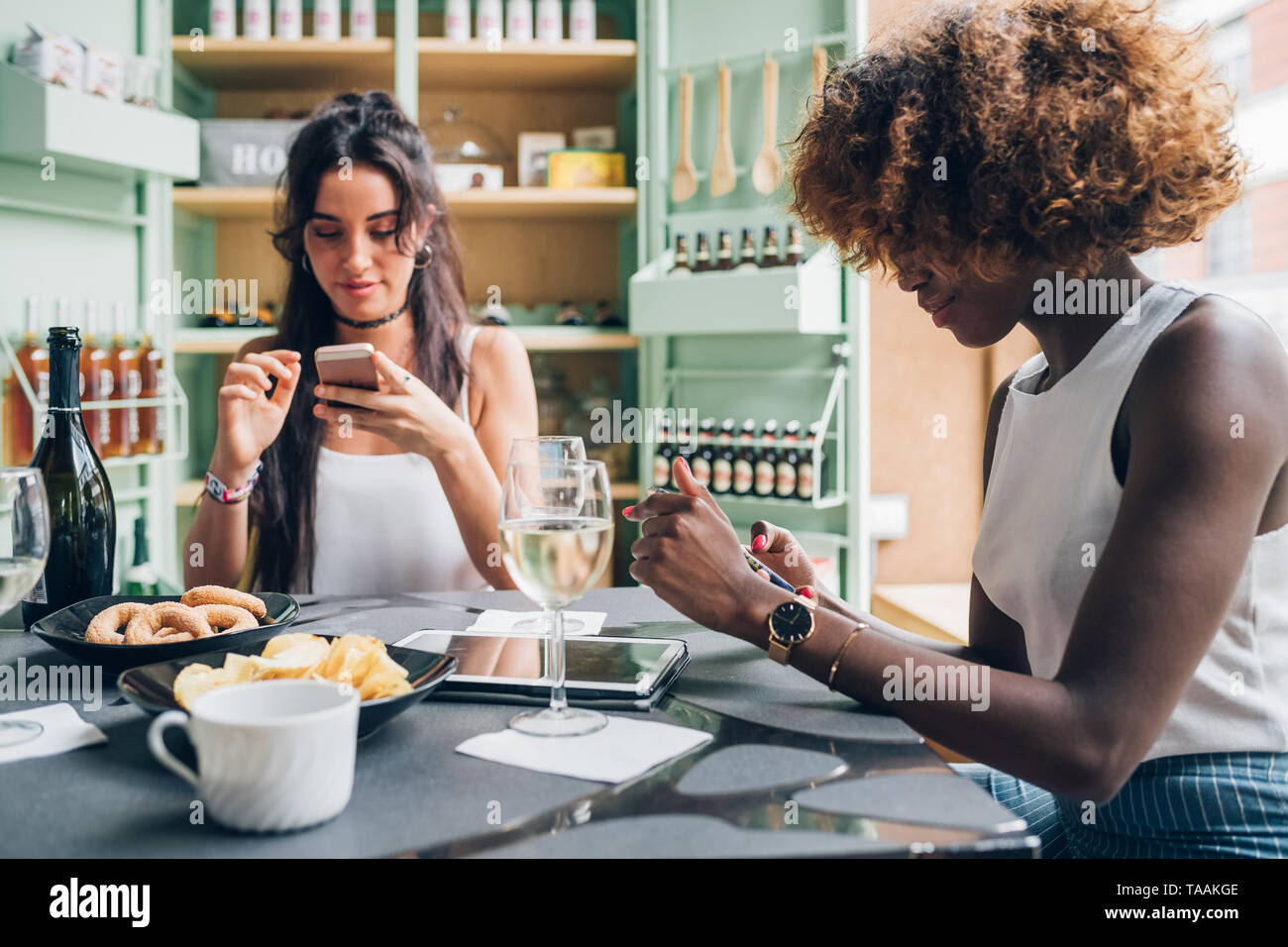 Zwei multirassischen junge Frauen chatten mit Smartphone und in modernen Pub sitzen - Verbindung von Jugend-, Technologie Stockfoto