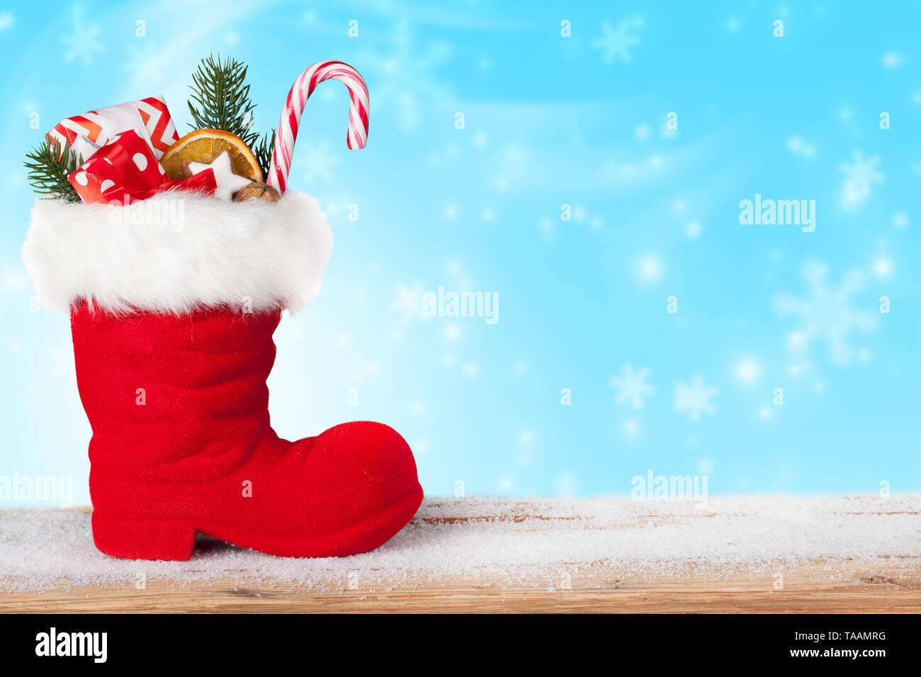 Santa Stiefel mit Süßigkeiten und Geschenke auf einem blauen Hintergrund mit fallenden Schneeflocken Stockfoto