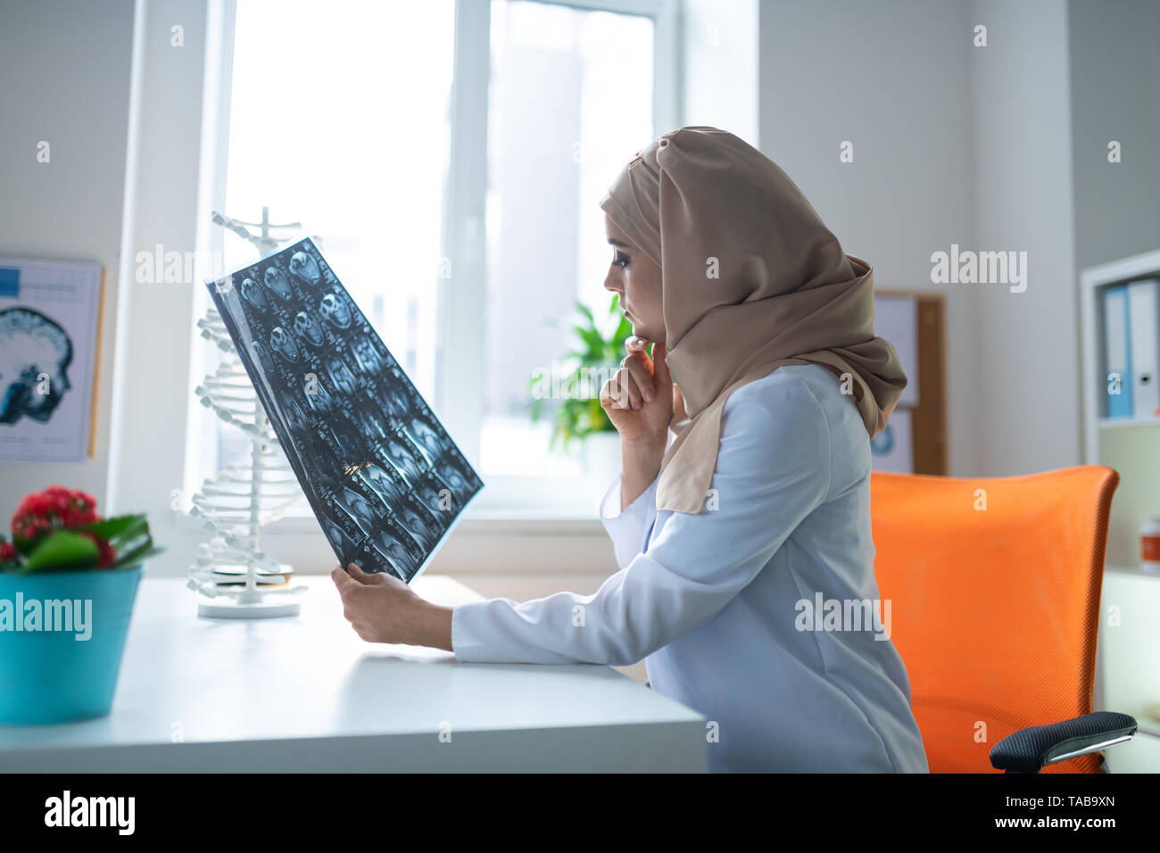 Arzt sitzen. Smart Ärztin tragen weiße Uniform und Kopftuch an einem Tisch sitzen Stockfoto