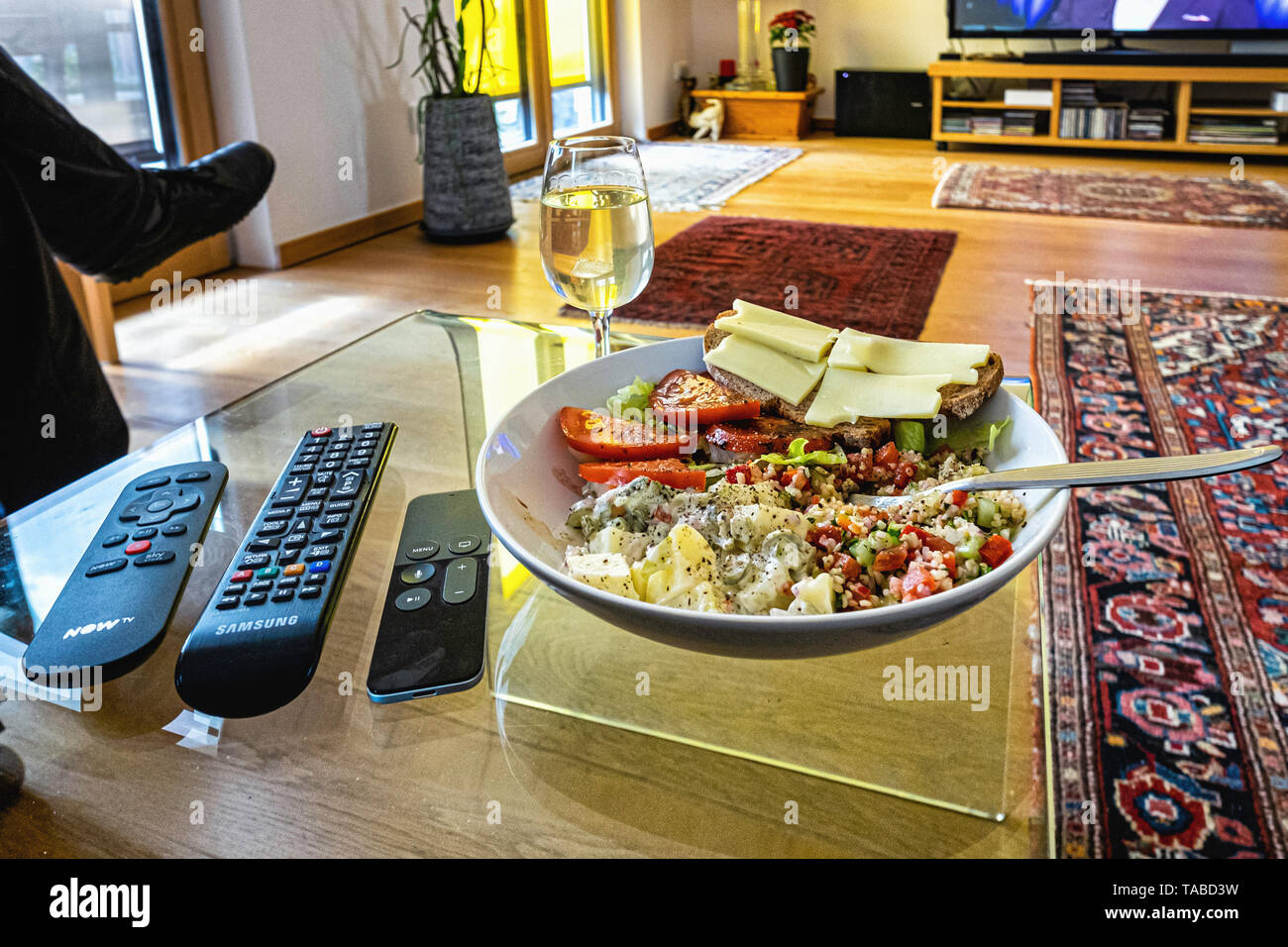 Gesunde Mahlzeit vor dem Fernsehen. Salate, Käse und Brot mit einem Glas Weißwein. Stockfoto