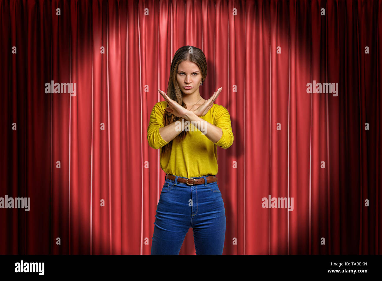 Junge bestimmt Frau in Jeans und gelbes Hemd, Ablehnung Geste auf rote Bühnenvorhänge Hintergrund Stockfoto