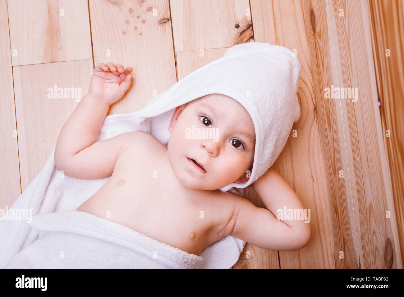 Baby Junge mit braunen Augen ist fünf Monate alt in einem weißen Handtuch mit Ohren auf hölzernen Hintergrund braun gehüllt. Stockfoto