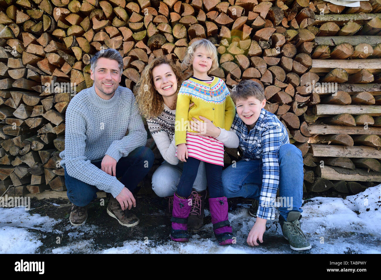 Portrait von Happy Family vor Stapel Holz im Winter Stockfoto