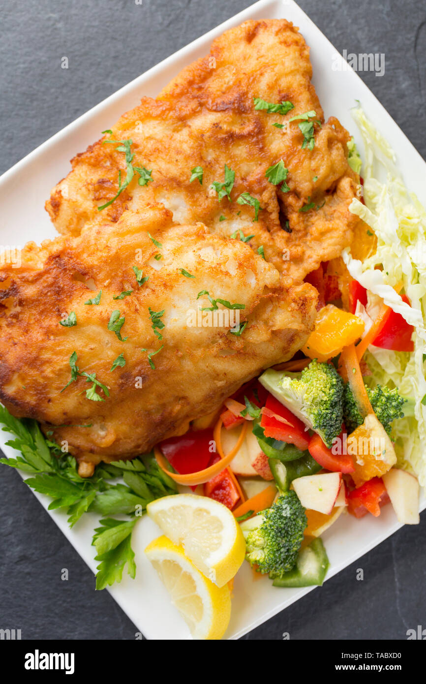 Zwei dicke Filets von Pollack Pollachius pollachius, dass tief in hausgemachter Teig gebraten und serviert mit Obst und rohem Gemüse. Die pollac Stockfoto