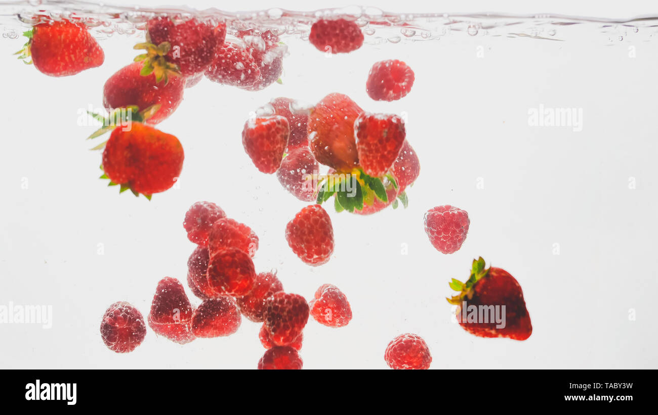 Closeup Bild der gemischte Beeren fallen und entsprechende/r im Wasser. Viele Himbeeren und Erdbeeren schwebend im Wasser vor weißem Hintergrund Stockfoto