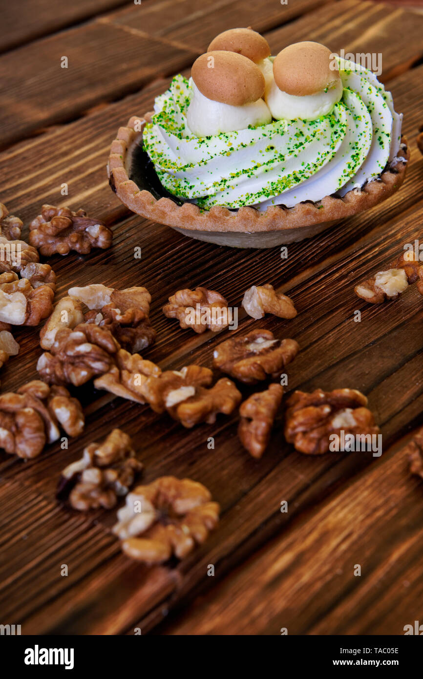 Auf dem hölzernen Tisch ist ein Kuchen in Form eines Korbes mit Protein Creme und Imitation von Pilzen. In der Nähe sind geschälte Walnüsse. Bild vertikal. Stockfoto