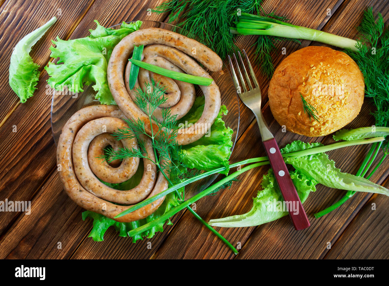 Gegrillte Würstchen, Mais bun und Gabel liegen auf einem Holz- Oberfläche mit Gruenen: Salat, Dill, Zwiebel und Petersilie. Picknick - Grill. Ansicht von oben Stockfoto