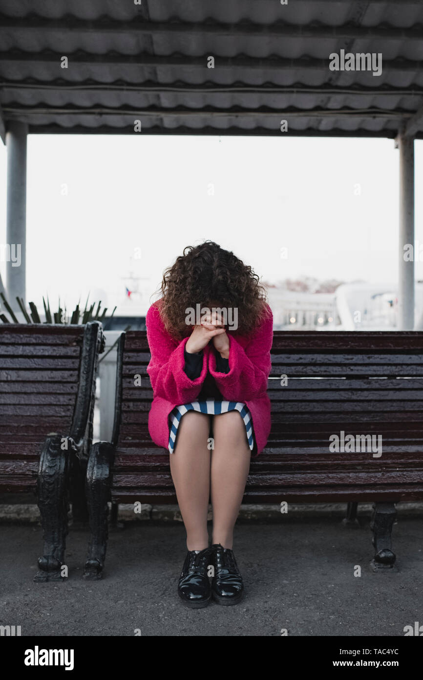 Frau mit lockigem Haar auf einer Bank sitzen Beten Stockfoto