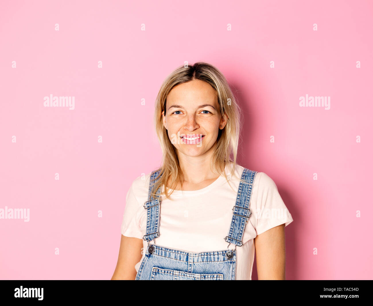 Portrait von lächelnden blonde Frau Latzhose tragen vor rosa Hintergrund Stockfoto