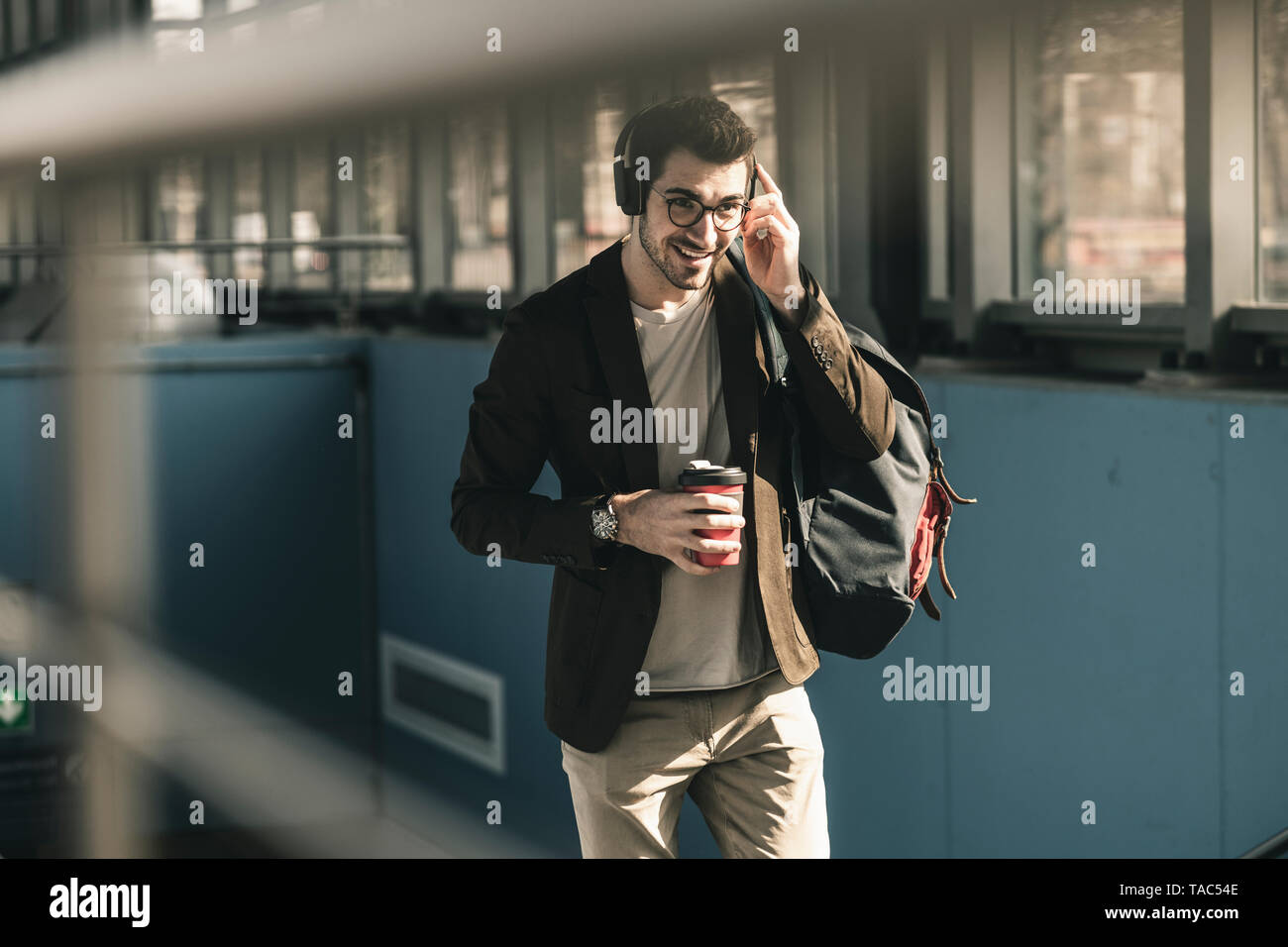 Lächelnden jungen Mann mit Kopfhörer, Handy und Kaffee zum Mitnehmen wandern an der Station Stockfoto
