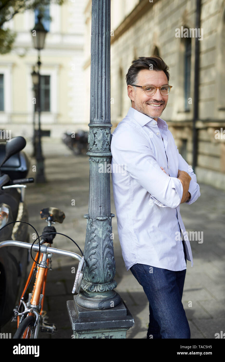 Portrait von lächelnden Geschäftsmann mit Fahrrad lehnte sich gegen Lamp Post in der Stadt Stockfoto