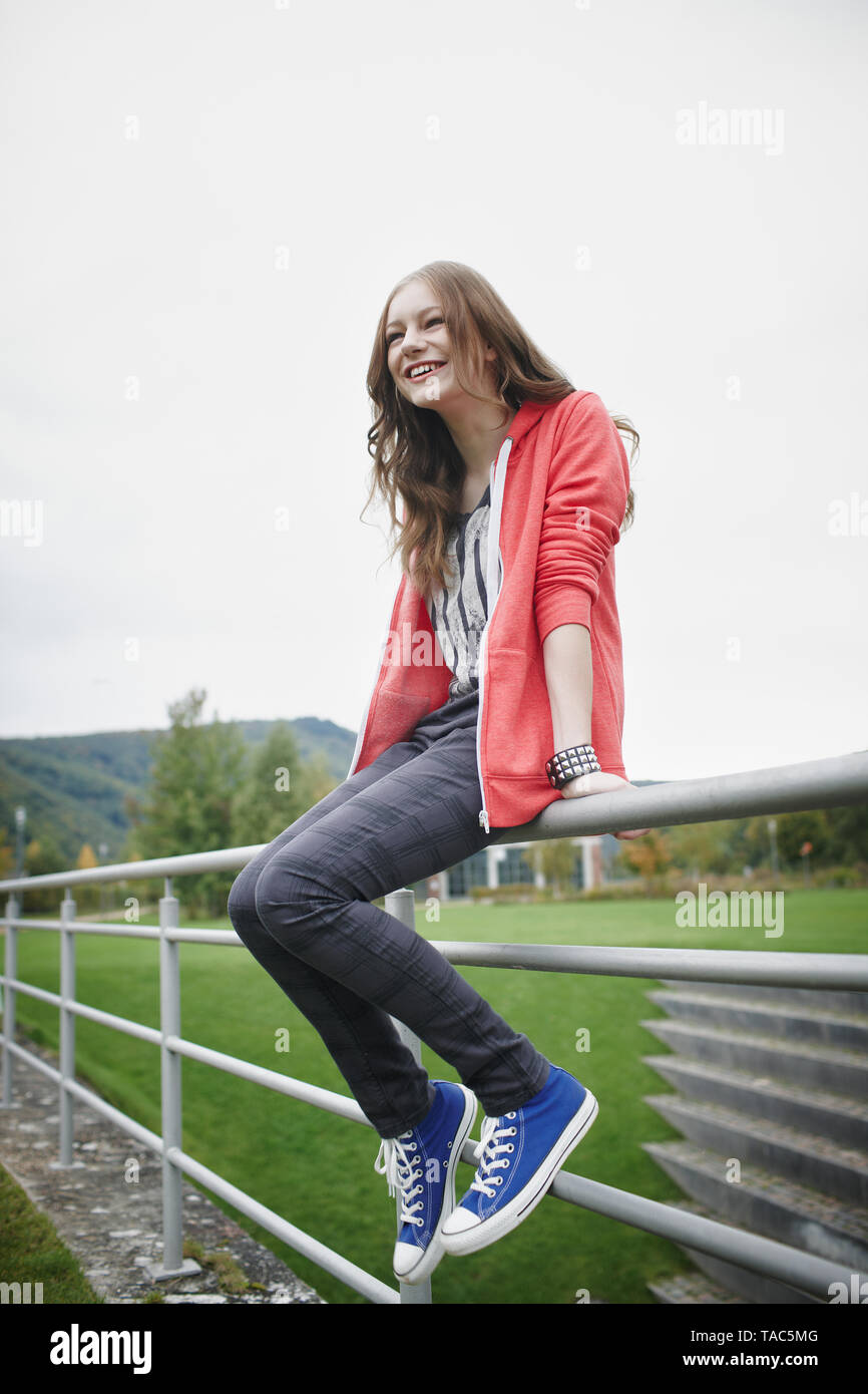 Glückliches junges Mädchen sitzt auf Zaun an einem Sportplatz Stockfoto