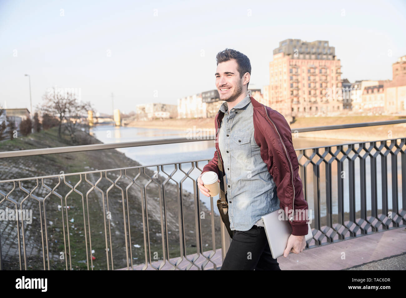Lächelnden jungen Mann mit Tablet, Tasche und Kaffee zum Mitnehmen auf einer Brücke in der Stadt Stockfoto
