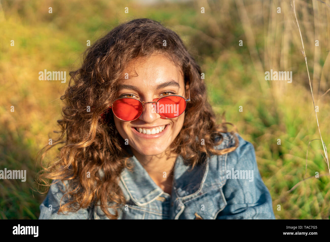 Porträt der glückliche junge Frau mit dem lockigen braunen Haar zu tragen rote Sonnenbrille Stockfoto