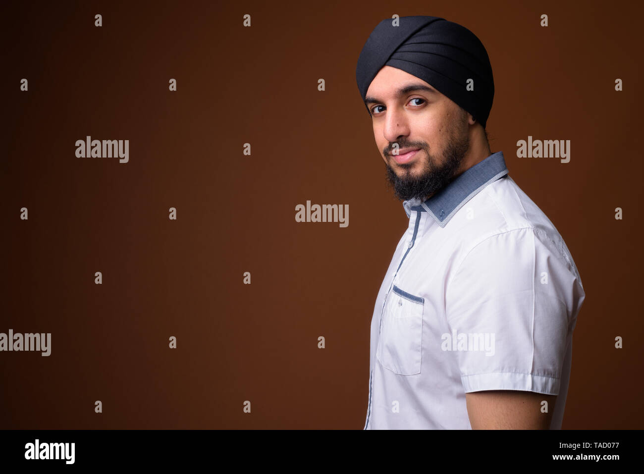 Studio erschossen Der junge Bartgeier indischen Sikh Mann, Smart Casual Kleidung gegen braunen Hintergrund Stockfoto