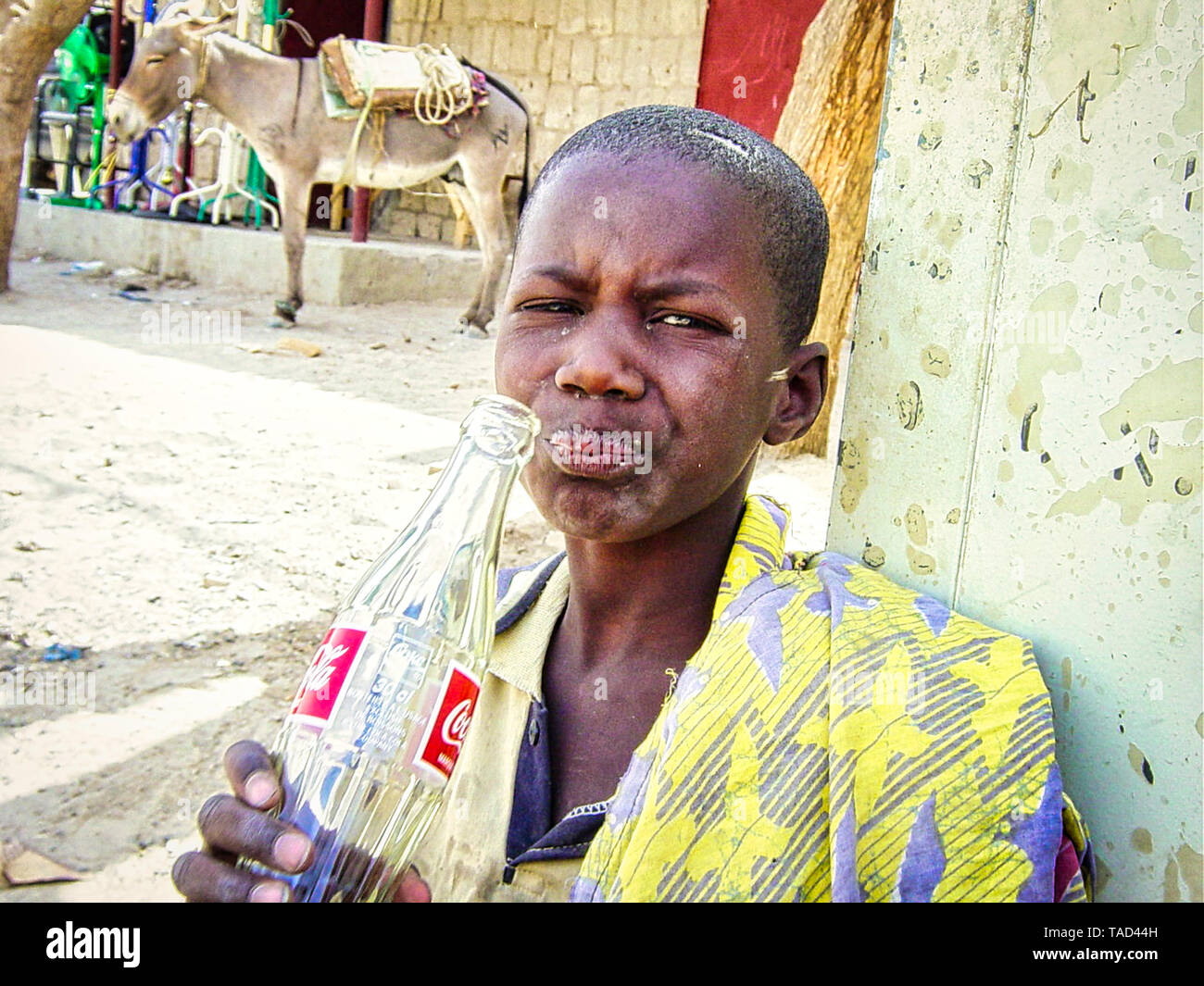 TIMBUKTU, MALI - Februar Circa, 2019. Nicht identifizierte arme Kind trinkt eine Coca-cola Flasche, gegeben durch Touristen in der Straße von Dorf in Mali Stockfoto