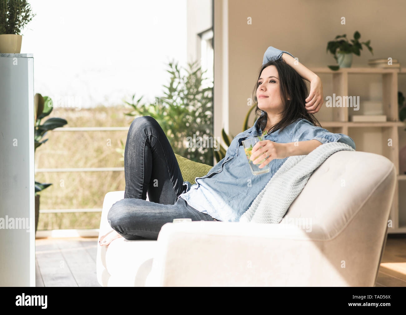 Lächelnde Frau mit einem Glas Wasser hineingegossen Sitzen auf der Couch zu Hause Stockfoto