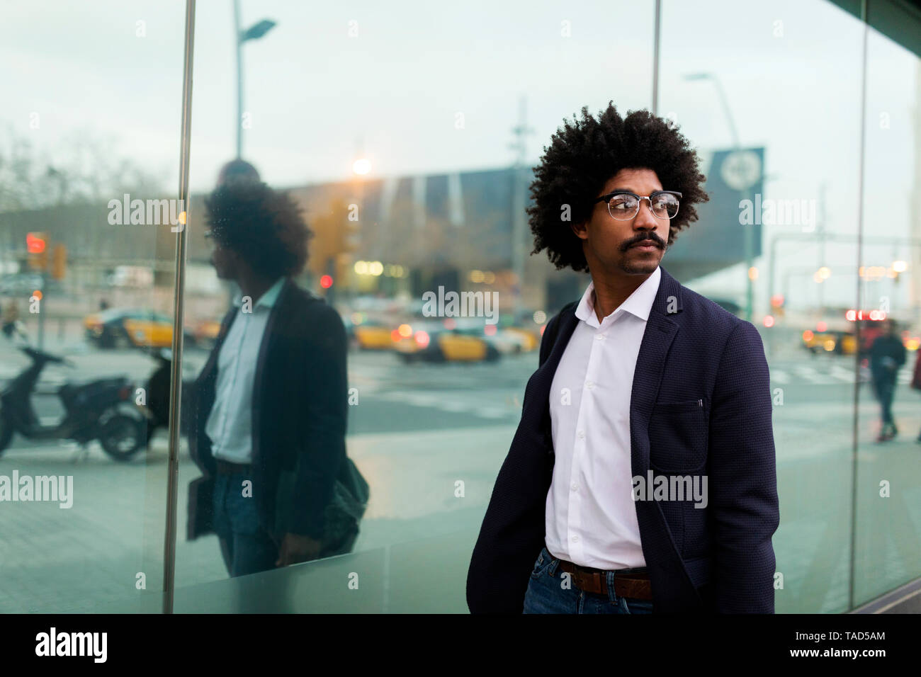 Spanien, Barcelona, Geschäftsmann unterwegs in der Stadt spiegelt sich in der Glasfront Stockfoto
