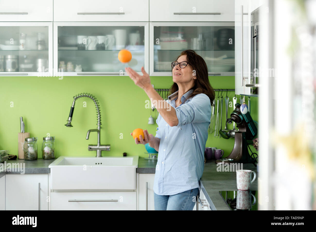 Reife Frau jonglieren mit Orangen in der Küche zu Hause. Stockfoto