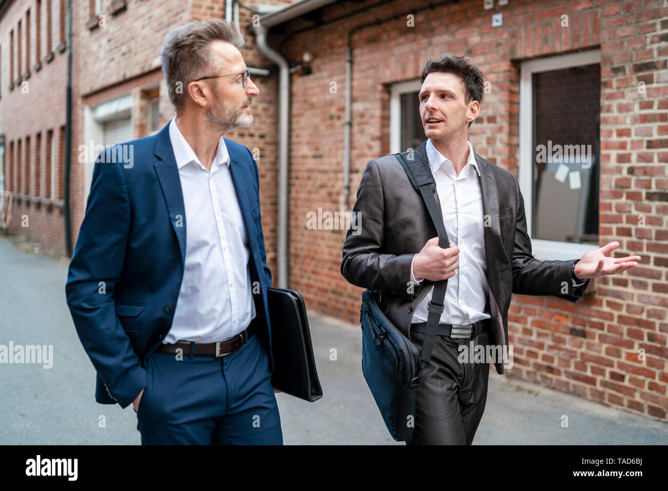 Zwei Geschäftsleute zu Fuß und im Gespräch mit einem alten Backsteingebäude Stockfoto