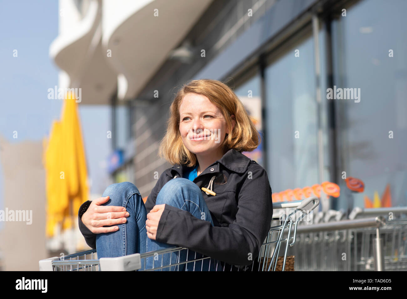 Portrait von lächelnden Frau in Warenkorb sitzen vor dem Supermarkt Stockfoto