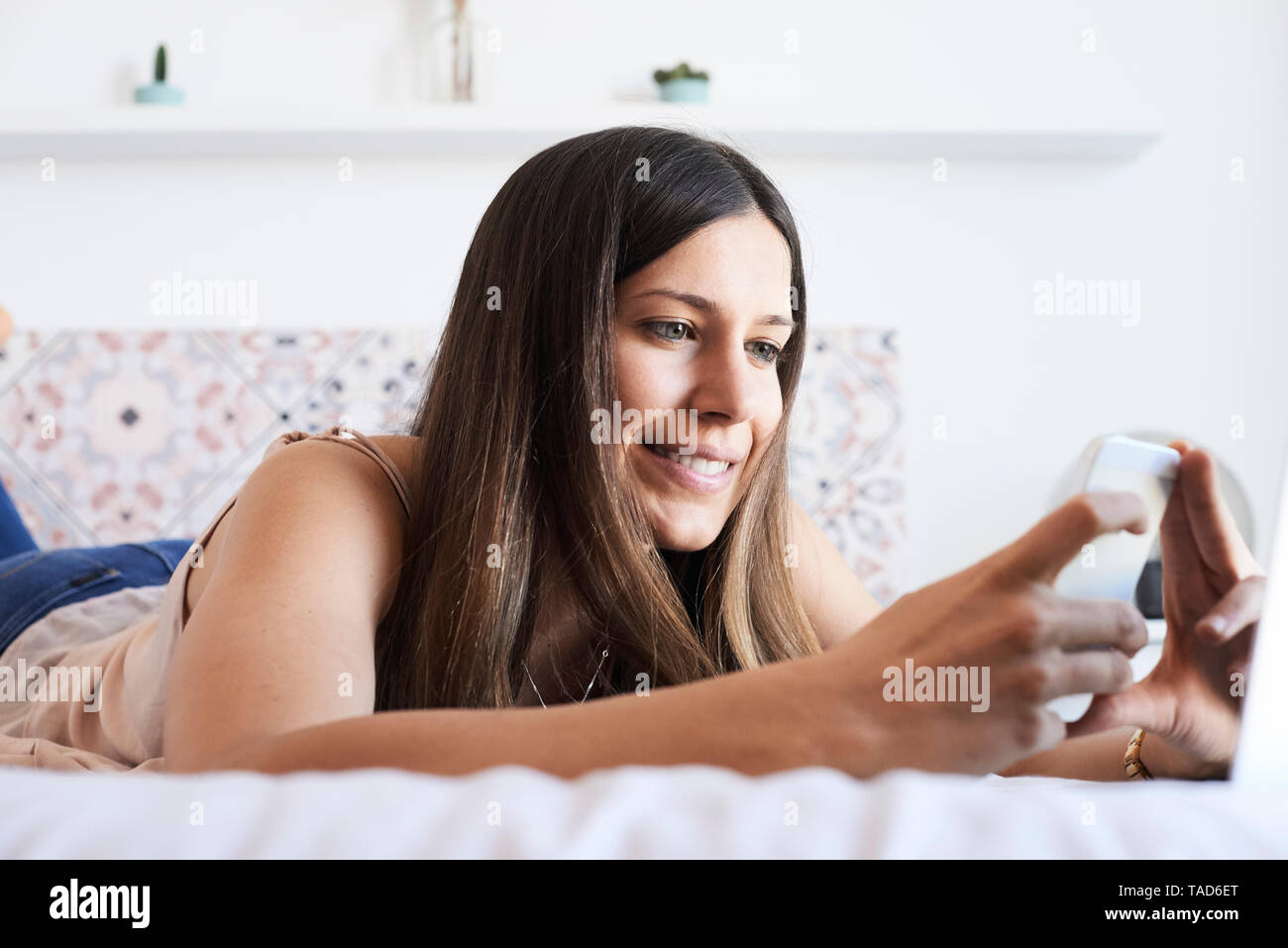 Portrait von lächelnden jungen Frau liegend auf Bett mit Smartphone Stockfoto