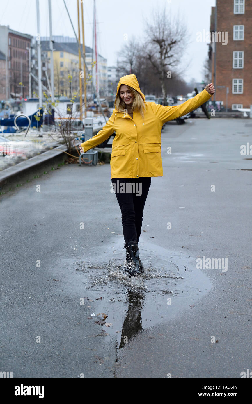 Dänemark, Kopenhagen, glückliche Frau in Pfützen am Hafen der Stadt springen Stockfoto