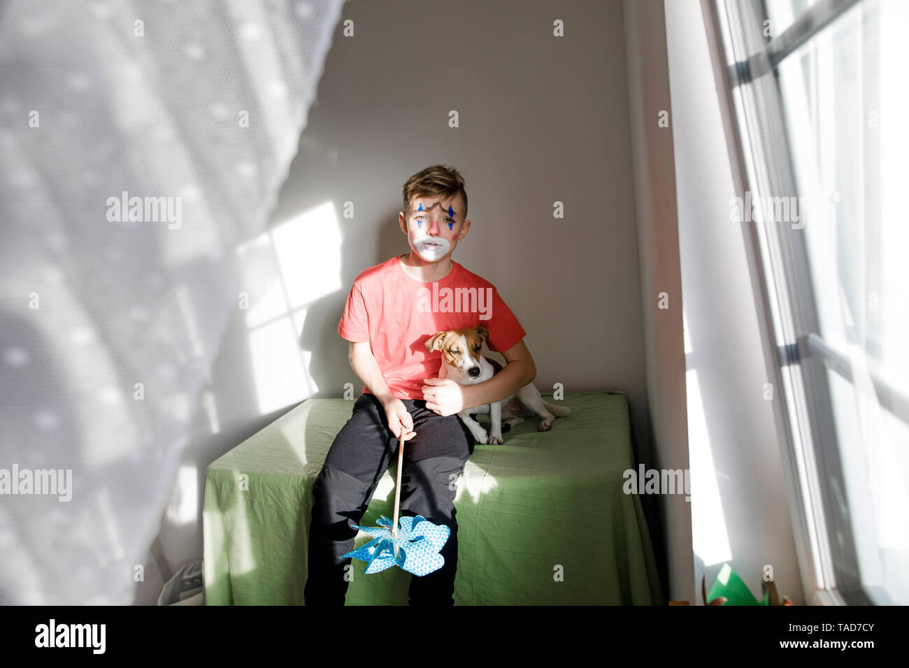 Portrait von Jungen, die sich wie ein Clown mit Hund und Stachelrad zu Hause Stockfoto